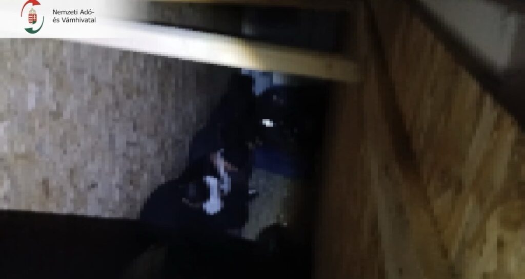 Szűk, OSB lapokkal burkolt rejtekhelyben összezsúfolva ülő emberek a teherautó rakterében.