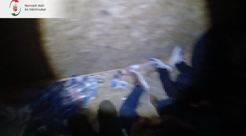 A rejtekhely padlóján fekvő emberek lábai és a körülöttük lévő zacskók, személyes tárgyak.