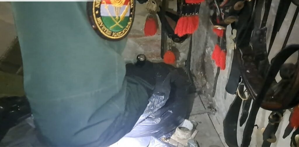 NAV egyenruhás pénzügyőr egy zsák dohány fölött, lószerszámokkal teli helyiségben.