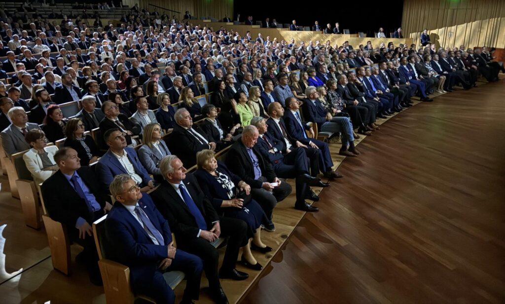 Nagy létszámú közönség ül a nézőtéren egy ünnepi rendezvényen, elegáns öltözetben, a színpad felé fordulva.