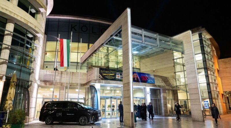 A debreceni Kölcsey Központ bejárata este, magyar zászlókkal és kivilágítva, elegáns vendégek érkeznek
