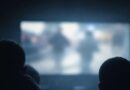 Háttal álló emberek sziluettjei egy elmosódott képernyő előtt félhomályban