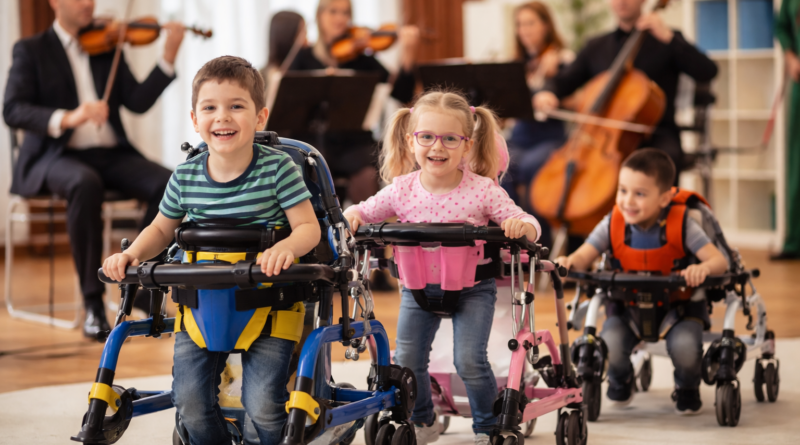 Mozgássérült gyerekek speciális járássegítő eszközökkel, háttérben zenészekkel