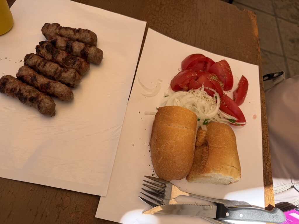 Grillezett görög kolbász, kebab friss paradicsommal, hagymával és kenyérrel tálalva.