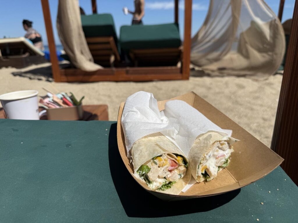 Friss zöldségekkel és csirkével töltött wrap egy tengerparti napágy mellett Thesszalonikiben.
