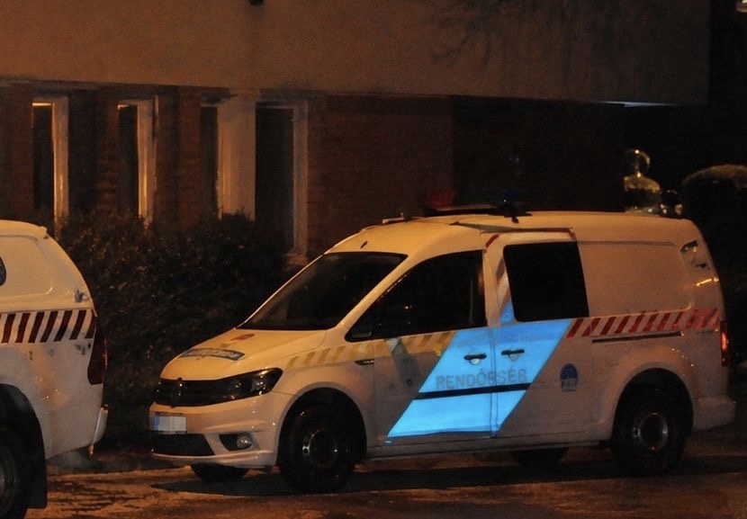 Rendőrségi kisbusz parkol éjszaka a Gödöllői Rendőrkapitányság előtt, a felgyújtott szolgálati autó közelében.
