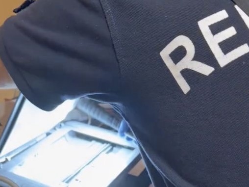 Rendőr digitális eszközöket vizsgál egy feltételezett okmányhamisító műhelyben.