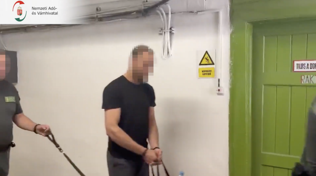 Elfogott férfit vezetnek a NAV munkatársai egy épület folyosóján