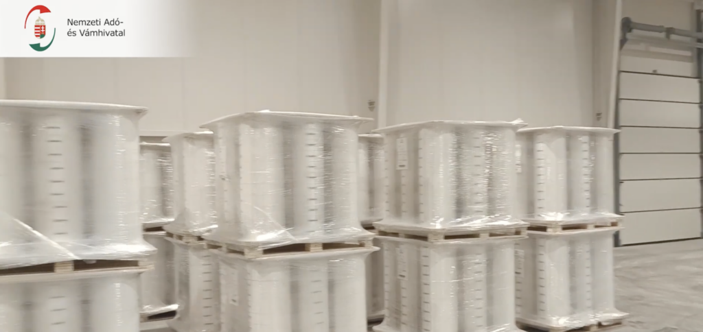 Fóliába csomagolt, raklapokra helyezett cigarettagyártási alapanyagok egy raktárépületben.