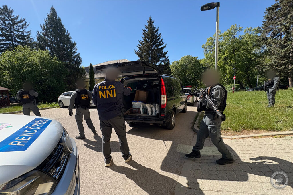NNI nyomozók és fegyveres rendőrök biztosítanak egy műveleti helyszínt.