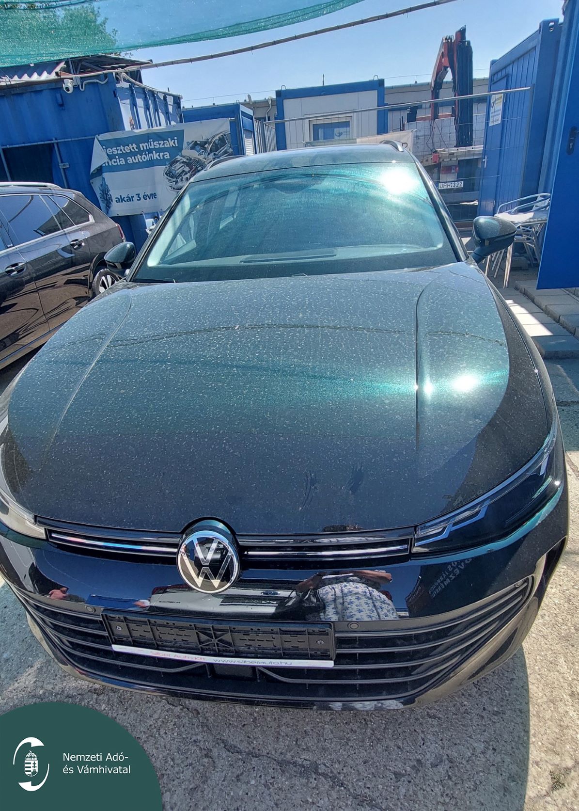 Sötét Volkswagen személyautó elölnézetből az autókereskedés udvarán.